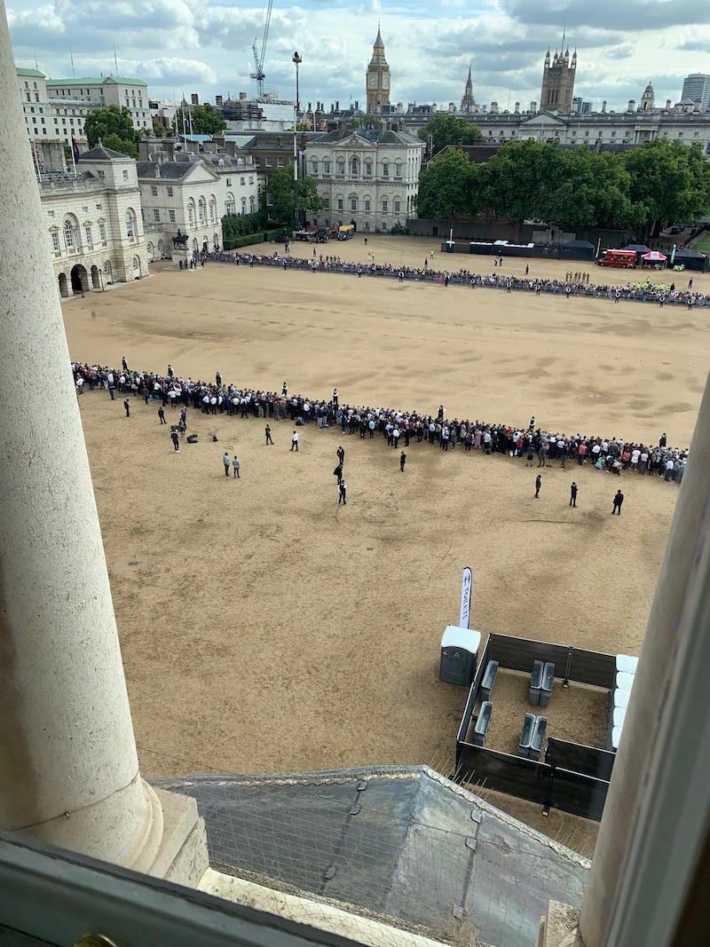 View of Horseguards Parade from upstairs in the Old Admiralty Building. Crowds await the procession. In the distance, the Houses of Parliament.